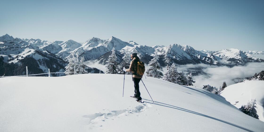 Wanderer mit Rucksack und Stöcken im Schnee vor Bergpanorama