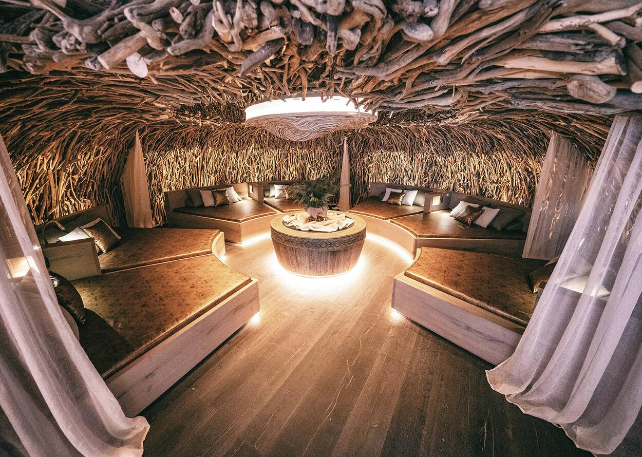 Spa-Raum mit Liegeflächen um einen runden Tisch, Decke mit Ästen und Wurzeln dekoriert