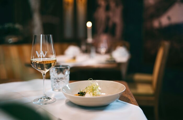 Ein stilvoll gedeckter Tisch mit einem Glas Weißwein und einem feinen Gericht in gemütlicher Restaurantatmosphäre.
