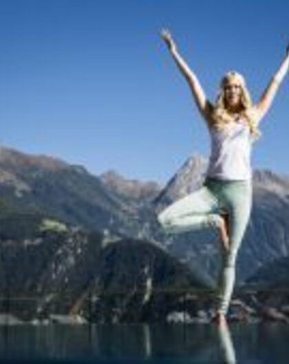 Frau macht Yoga-Baum vor Bergpanorama