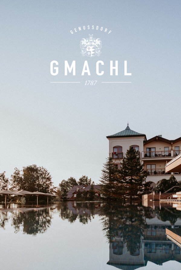 Spiegelung eines Gebäudes im Wasser unter blauem Himmel mit Logo Gmachl