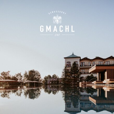 Spiegelung eines Gebäudes im Wasser unter blauem Himmel mit Logo Gmachl