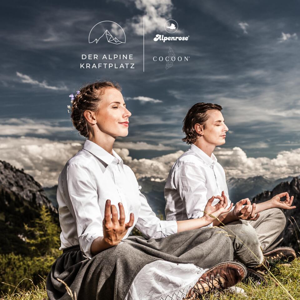 Frau und Mann meditieren in Berglandschaft vor Bergspitze