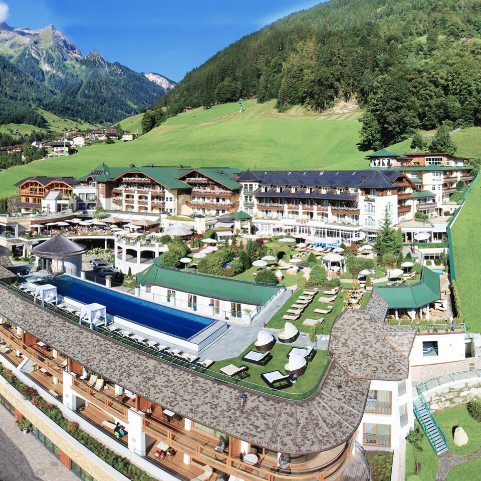 Hotelanlage mit Pool vor grünen Hügeln und Bergen im Sommer
