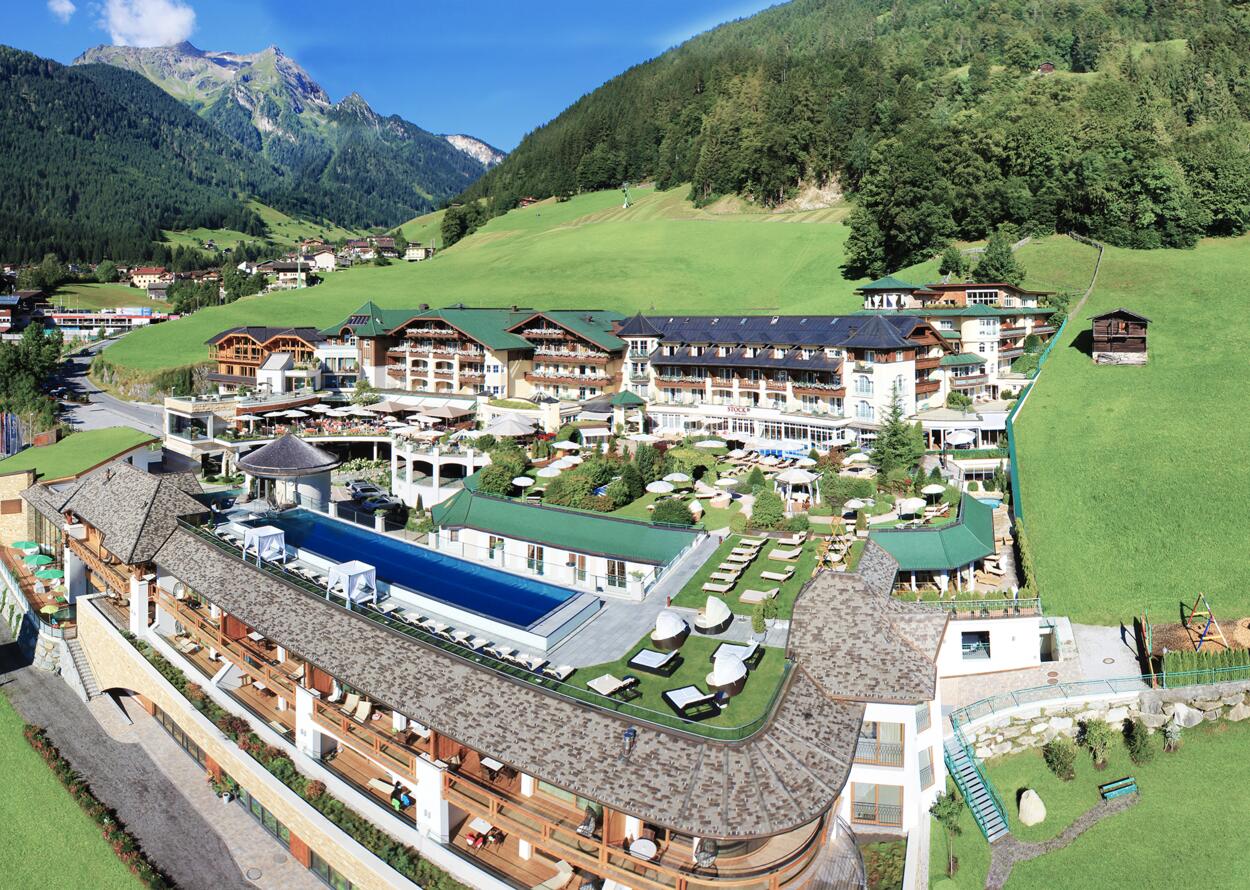 Hotelanlage mit Pool vor grünen Hügeln und Bergen im Sommer