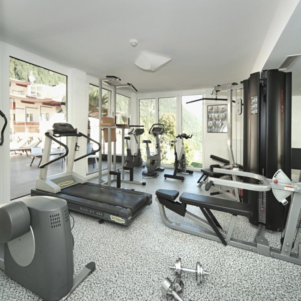 Heller Fitnessraum mit Geräten wie Laufband, Hantelbank und Fahrrädern