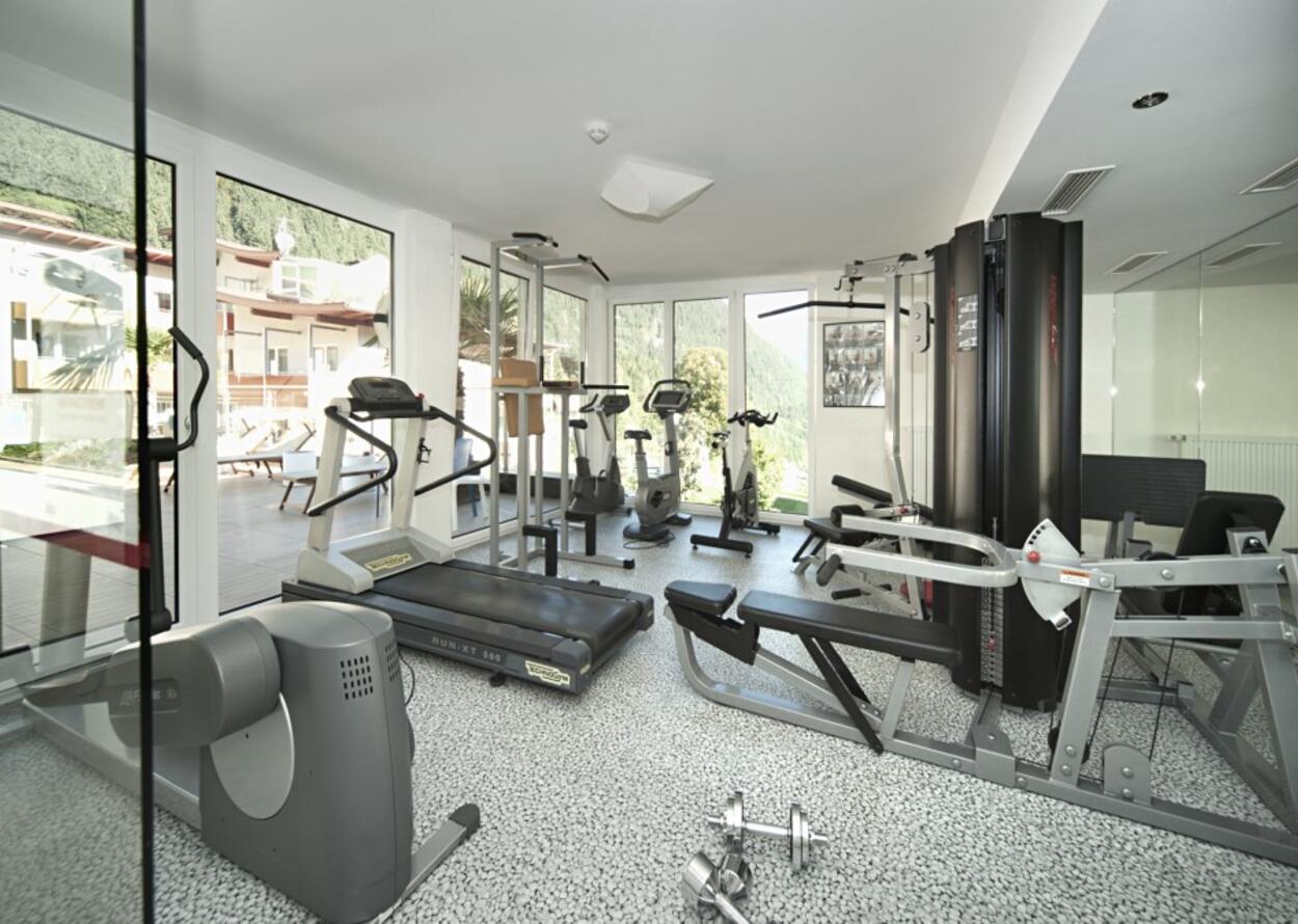 Heller Fitnessraum mit Geräten wie Laufband, Hantelbank und Fahrrädern