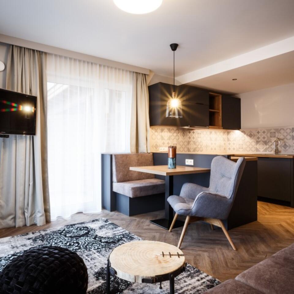Wohnzimmer mit Esstisch, Sessel, Teppich und Küchenzeile in modernem Design