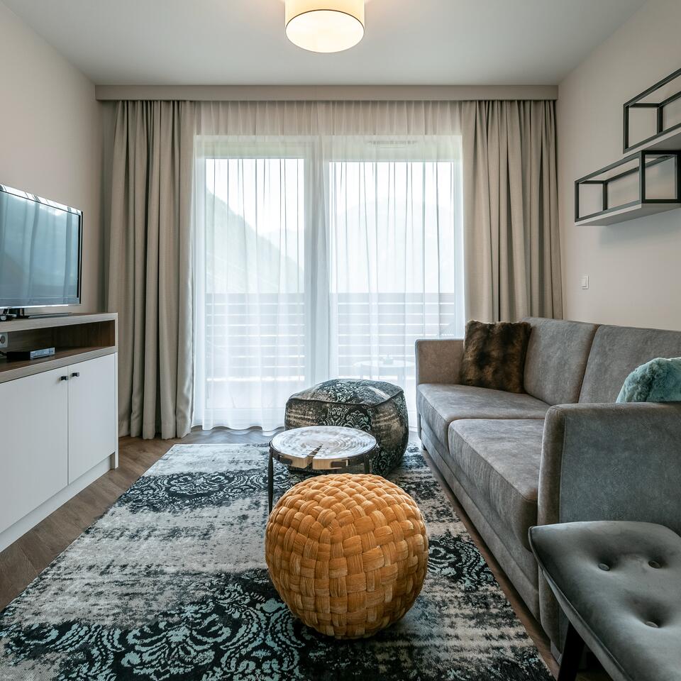 Wohnzimmer mit grauem Sofa, Teppich, Poufs und Balkontür