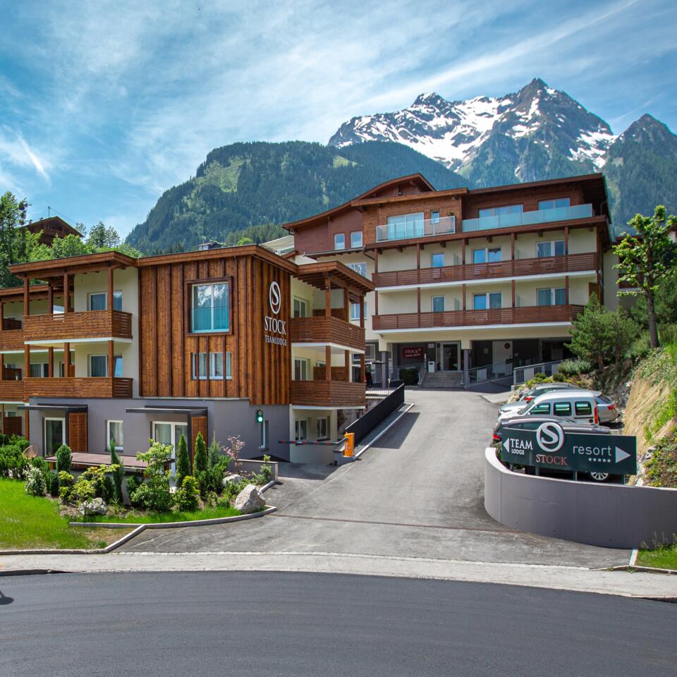 Hotelanlage in den Bergen mit grüner Wiese und geparktem Oldtimer